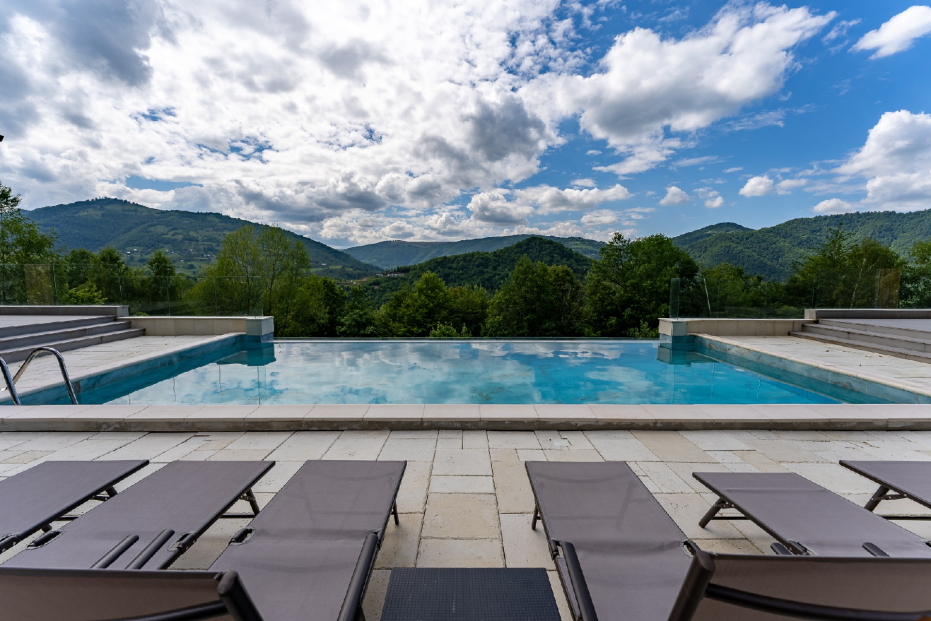 Piscina exterioară a Cabanelor Carmel, cu șezlonguri și panorama munților împăduriți din Muntele Rece